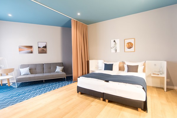 Aufnahme mit Blick auf das gemütliche Bett und Sofa in einem Hotelzimmer im about:berlin